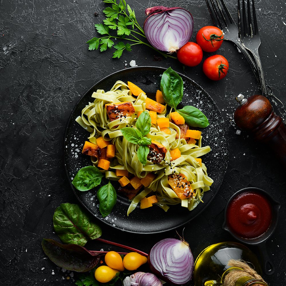 Pasta with pumpkin and spinach in a black plate on a black background. Top view. Free space for your text.